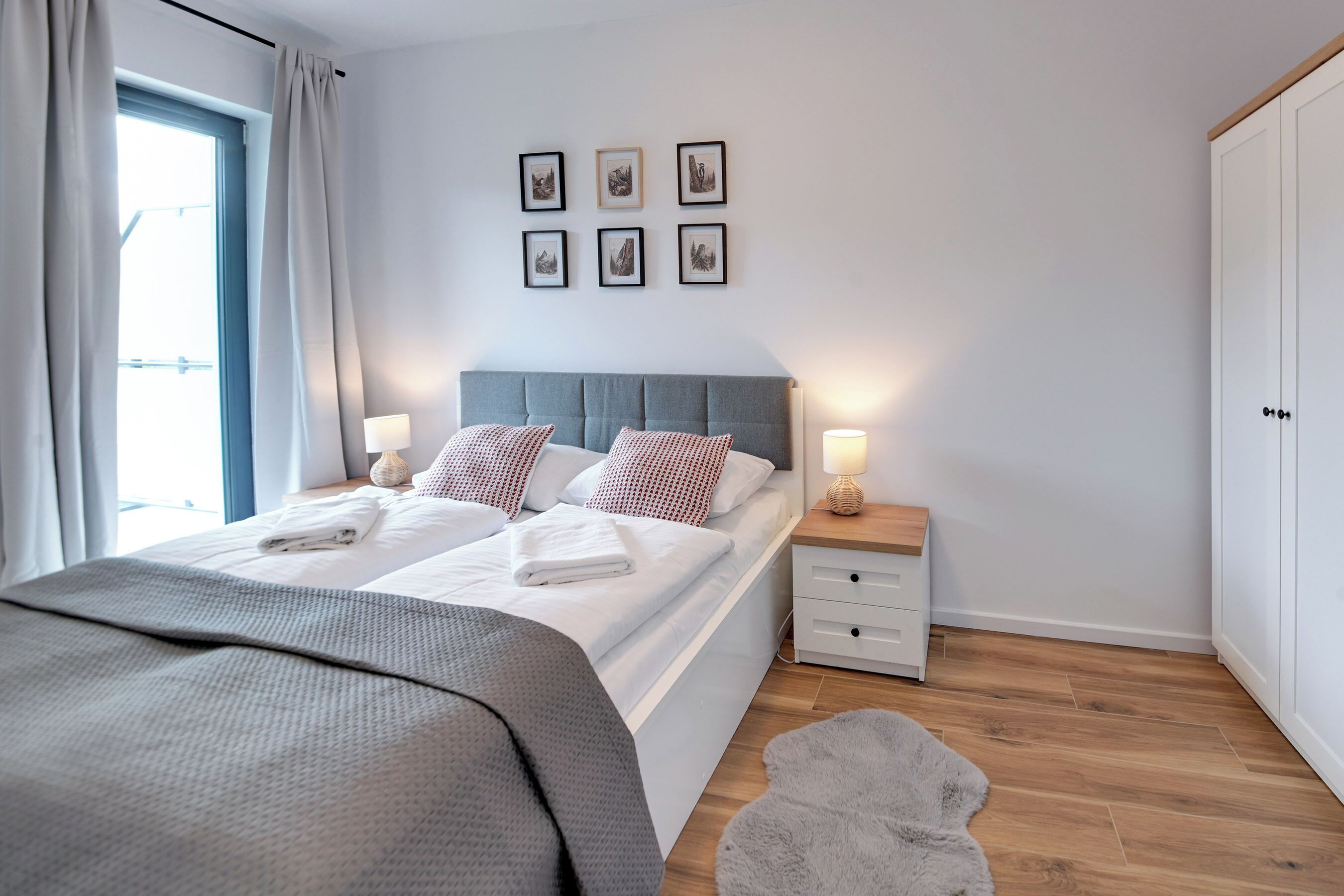A modern bedroom with a double bed, bedside tables with lamps, a grey headboard, and a wardrobe.