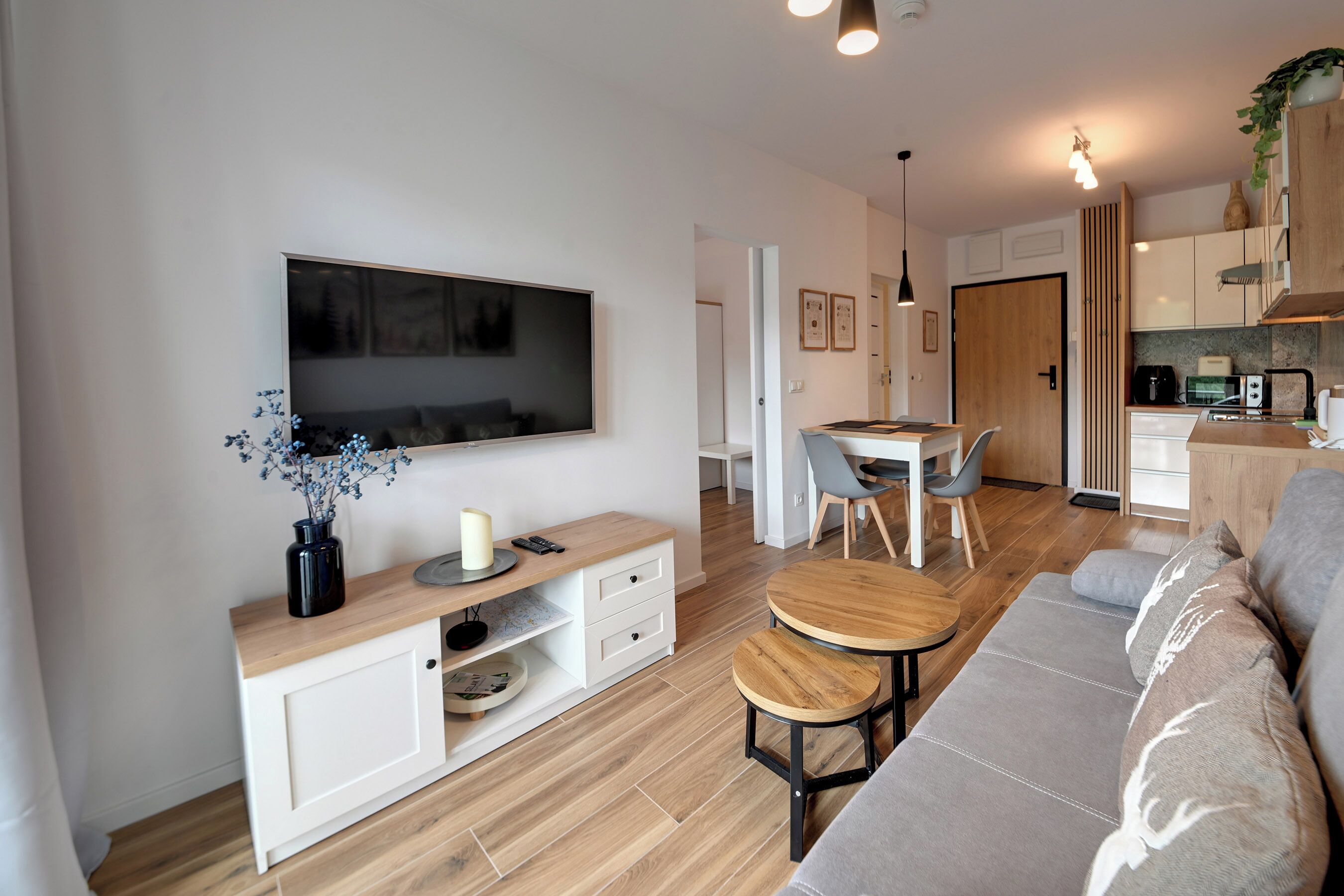 A modern living room with a flat-screen TV, a coffee table, a sofa, and a dining area with a table and chairs.