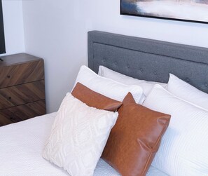 A bed with white bedding and two pillows, one white and one brown, against a grey headboard. - City Luxury @ Smart Pricing + Parking + Family-Friendly (Cincinnati)