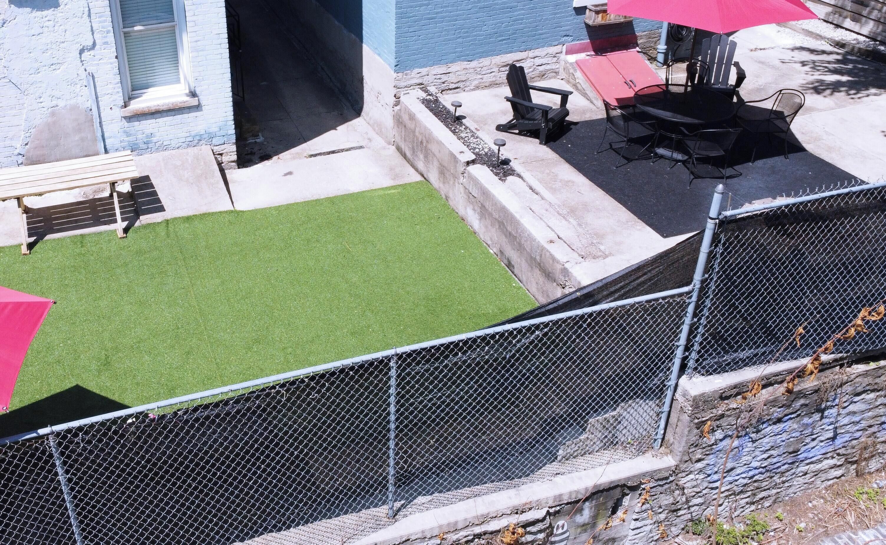 Un espacio exterior vallado con césped artificial, una zona de barbacoa y un área de estar con sillas y mesas.