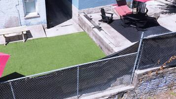 Un espacio exterior vallado con césped artificial, una zona de barbacoa y un área de estar con sillas y mesas.