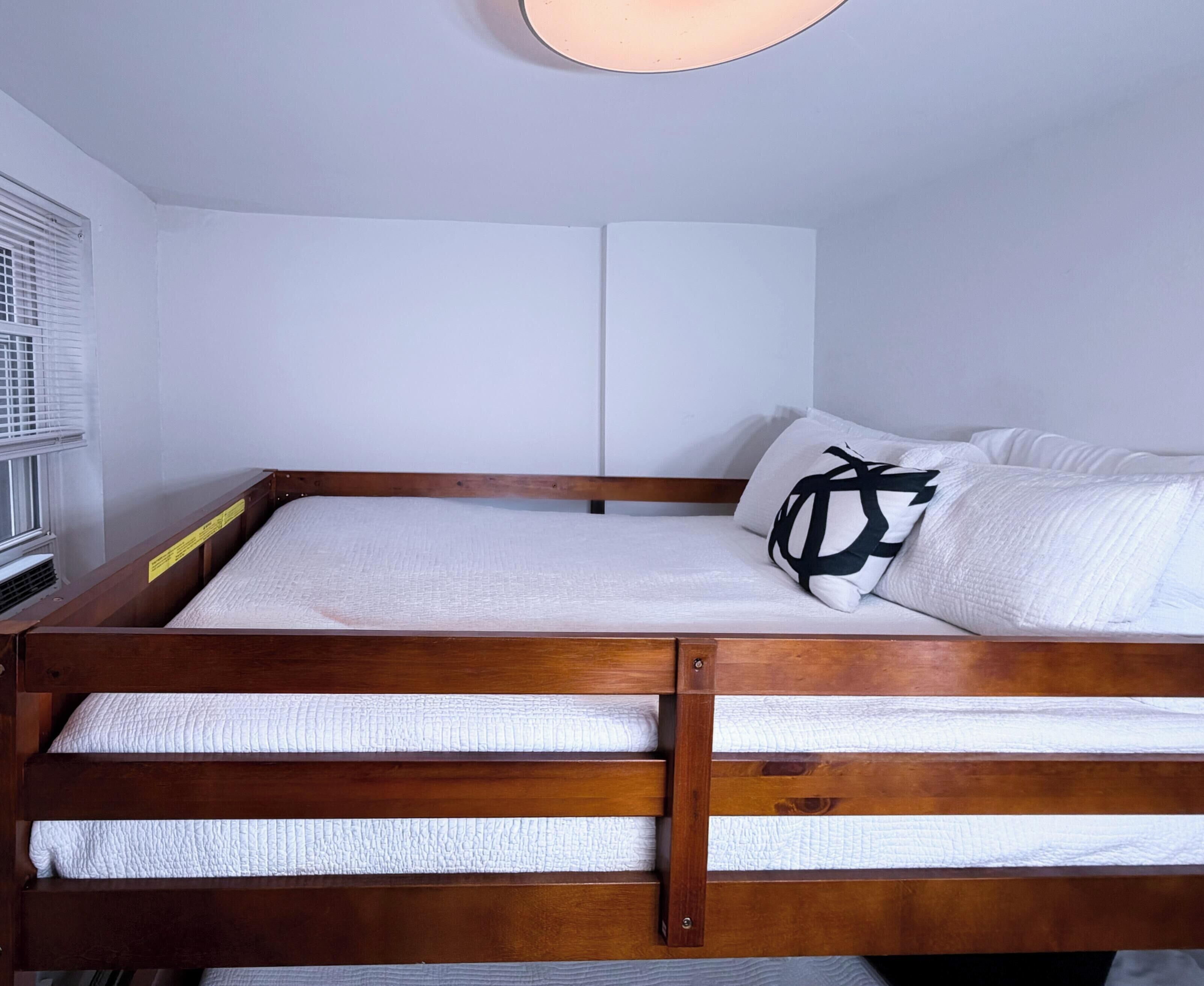 A single bed with a wooden frame, white bedding, and a black pillow with a geometric design.
