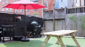 En baghave med grill, et træbord og en rød parasol.