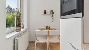 A small kitchen with a window, a radiator, a table with chairs, and a refrigerator. - Stylish Studio · Augustaplatz · Kurpark · GOP (Bad Oeynhausen)