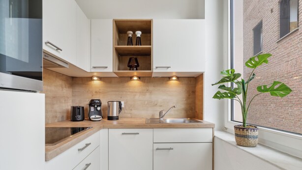 A modern kitchen with white cabinets, a wooden countertop, a built-in oven, a coffee maker, and a potted plant by the window. - Stylish Studio · Augustaplatz · Kurpark · GOP (Bad Oeynhausen)