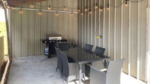 An outdoor patio with a glass-top table surrounded by wicker chairs, a grill, and string lights. - Eclectic 3-bedroom home in exciting MidCity filled with local art! (Baton Rouge)