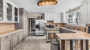 A modern kitchen with white cabinetry, a stainless steel refrigerator, and a wooden island. - Eclectic 3-bedroom home in exciting MidCity filled with local art! (Baton Rouge)