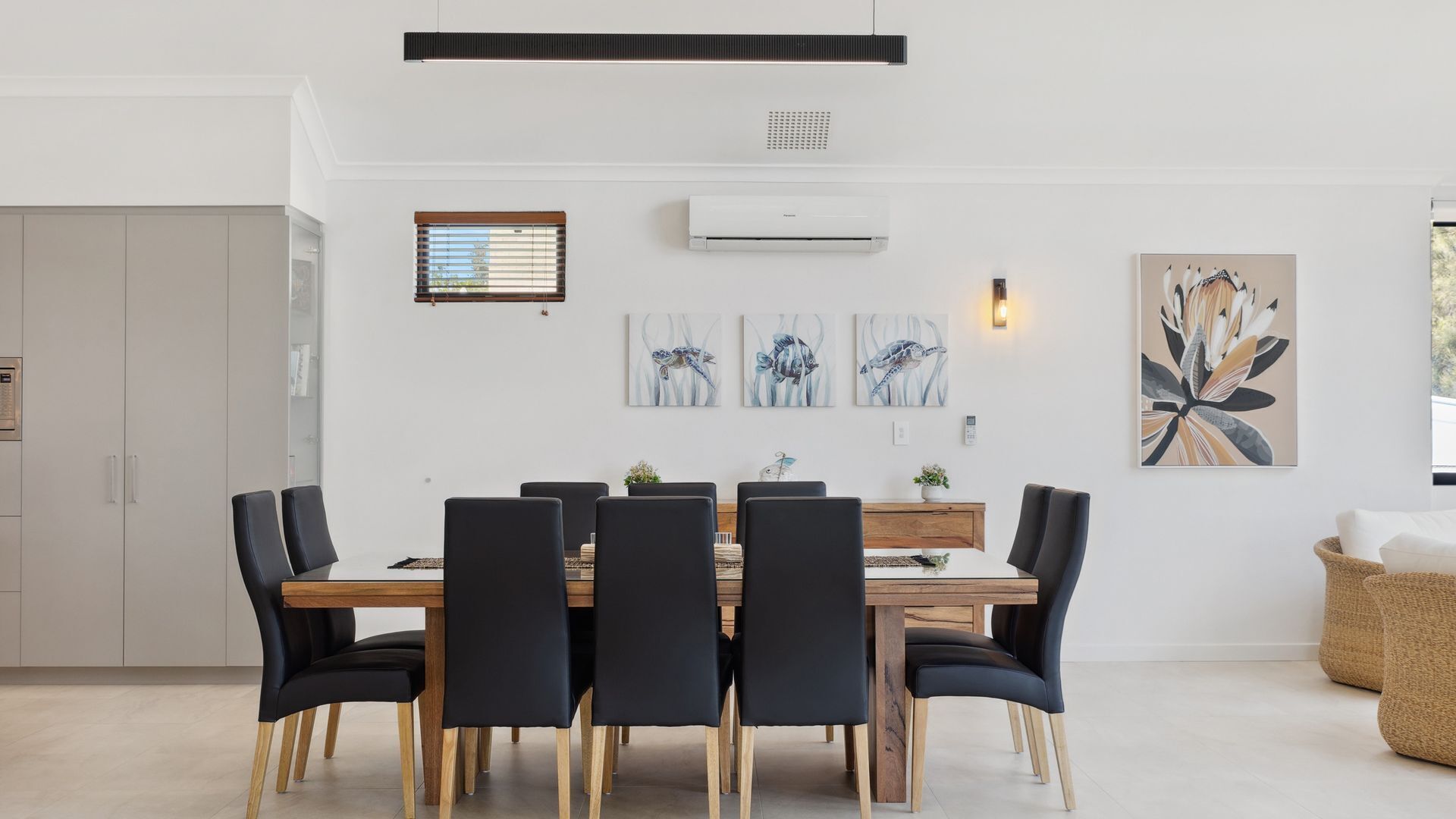 A modern dining area with a wooden table and black chairs, a built-in air conditioning unit, and wall-mounted artwork.