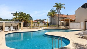 A swimming pool with lounge chairs and palm trees, surrounded by buildings with tiled roofs.