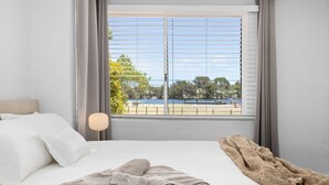A bedroom with a bed, a lamp, and a view of a lake and trees through the window.
