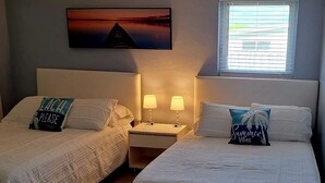 A hotel room with two beds, each with a pillow, a nightstand with lamps, and a painting on the wall. - Private duplex house with WI-FI, TVs, BBQ Parking ,enjoy a peaceful Getaway (Cutler)