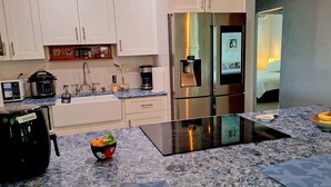 A modern kitchen with white cabinets, a stainless steel refrigerator, a built-in stove, and a granite countertop. - Private duplex house with WI-FI, TVs, BBQ Parking ,enjoy a peaceful Getaway (Cutler)