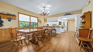 Un comedor amplio con una gran mesa de madera y sillas a juego, una araña y vistas al exterior.