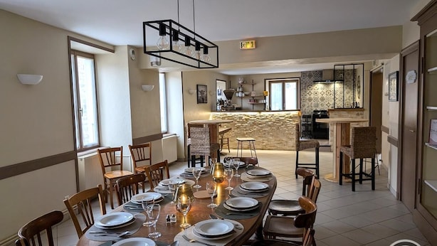 Un comedor con una mesa larga dispuesta para una comida, sillas de madera y una lámpara colgante moderna.