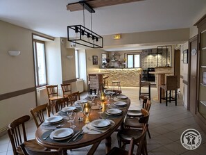 Un comedor con una mesa larga dispuesta para una comida, sillas de madera y una lámpara colgante moderna.