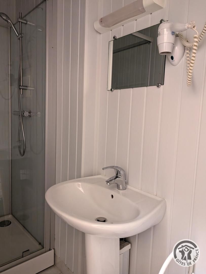 A bathroom with a glass shower enclosure, a white sink with a modern faucet, and a hairdryer mounted on the wall.