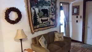 Un salon avec un canapé, une lampe, une tapisserie murale et une porte.