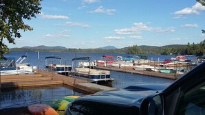 Un port de plaisance avec des bateaux amarrés, une voiture au premier plan et un lac avec des montagnes en arrière-plan.