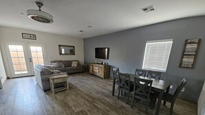 A living room with a sofa, a TV, a dining table with chairs, and a wooden floor. - Cozy spacious modern guest house in charming Queen Creek with AC & WiFi (Queen Creek)