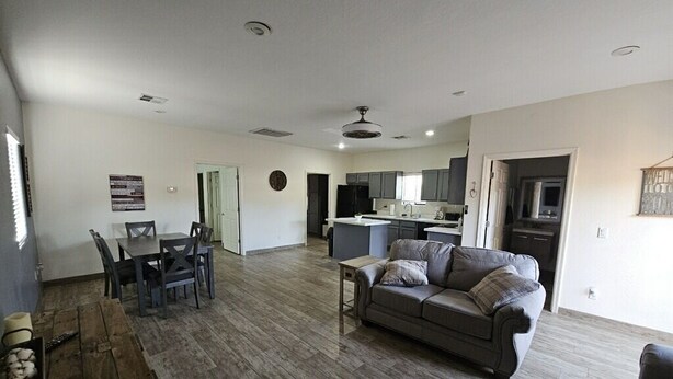 A spacious living room with a large grey sofa, a dining area with a table and chairs, and a kitchen area with modern appliances. - Cozy spacious modern guest house in charming Queen Creek with AC & WiFi (Queen Creek)
