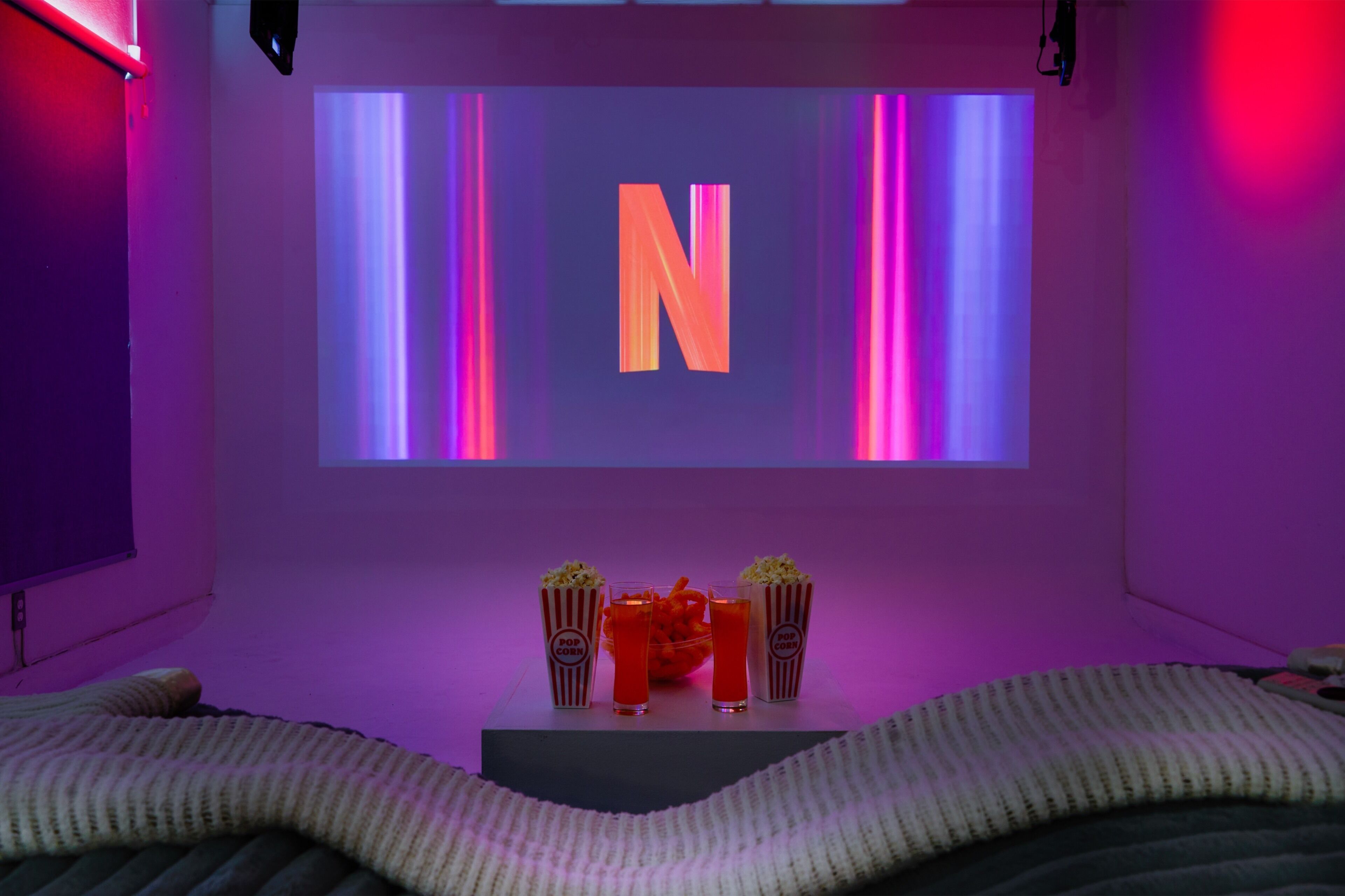 A room with a large screen displaying a letter 'N', a popcorn container, a drink, and a snack bowl.