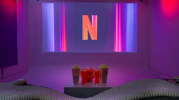 A room with a large screen displaying a letter 'N', a popcorn container, a drink, and a snack bowl.
