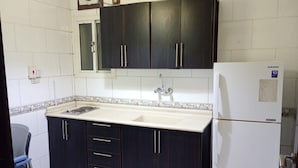 A compact kitchen with dark cabinets, a white countertop, a built-in sink, and a white refrigerator. - Asalat Alhamra (Jeddah)