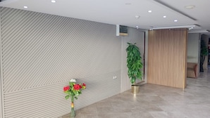 A modern reception area with a patterned wall, a potted plant, and a vase of red flowers. - Asalat Alhamra (Jeddah)
