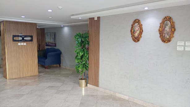 A reception area with a blue sofa, a potted plant, and two ornate wall mirrors. - Asalat Alhamra (Jeddah)