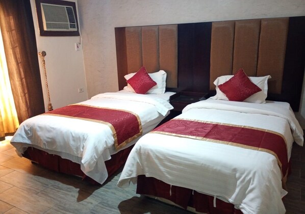 Two beds with white and red bedding, a wooden headboard, and a wall-mounted air conditioner.