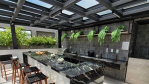 An outdoor kitchen area with a marble countertop, wooden chairs, and a metal ceiling structure. - Skylux Studio Museum of Tomorrow, Rio de Janeiro Wonderful and Safe.  (Centro Rio de Janeiro)