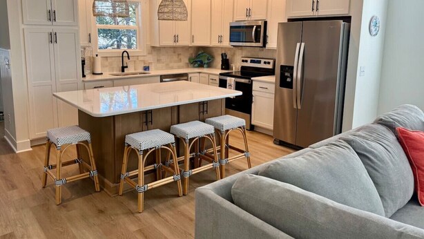 Una cocina moderna con armarios blancos, una isla central con taburetes, electrodomésticos de acero inoxidable y un ventanal con vistas.