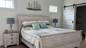 Un dormitorio con una cama de madera, dos mesitas de noche con lámparas, una decoración náutica en la pared y una puerta corrediza.