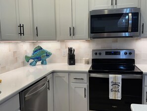 A modern kitchen with white cabinets, a stainless steel microwave, a black oven, and a fish-shaped decorative item on the counter. - Seagull`s Song (Oak Island)