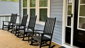 Un porche con cuatro sillas Adirondack negras y una terraza de madera.