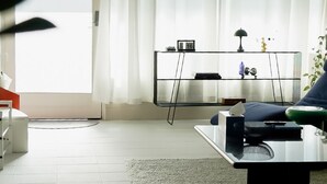 Een moderne woonkamer met een glazen salontafel, een bank, een bijzettafeltje en een glazen kast met decoratieve objecten.