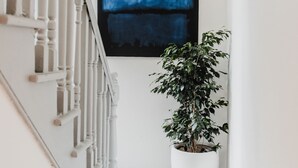 Een trap met witte spijlbalken, een groot abstract blauw schilderij aan de muur en een potplant.