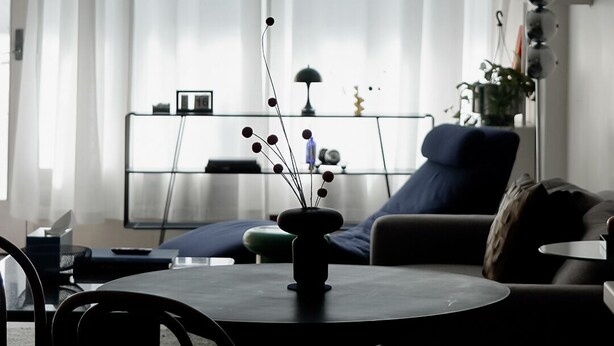 Een kamer met een ronde tafel, een hangende papieren lantaarn, een bank en een raam met gordijnen.