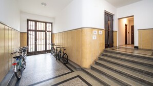 Un pasillo limpio y bien iluminado con una escalera que sube a otro piso, una puerta con un letrero y bicicletas estacionadas contra la pared.