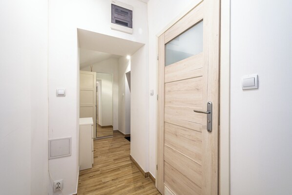 A hallway with a wooden door, a light switch, and a thermostat on the wall.
