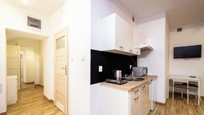 Una cocina moderna con armarios blancos, encimera de granito, microondas y hervidor. Hay una pequeña zona de comedor con una mesa y sillas.