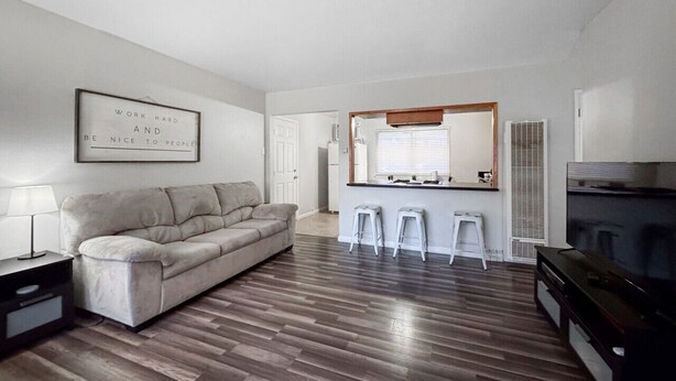 Una sala de estar moderna con un sofá, un televisor y una cocina al fondo.