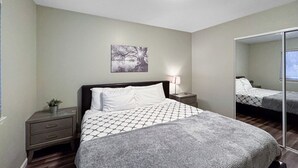 Un dormitorio con cama, mesita de noche, espejo e imagen colgada en la pared.