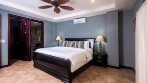 Une chambre à coucher avec un lit en bois foncé, deux tables de chevet avec des lampes, un ventilateur de plafond et un appareil de climatisation.