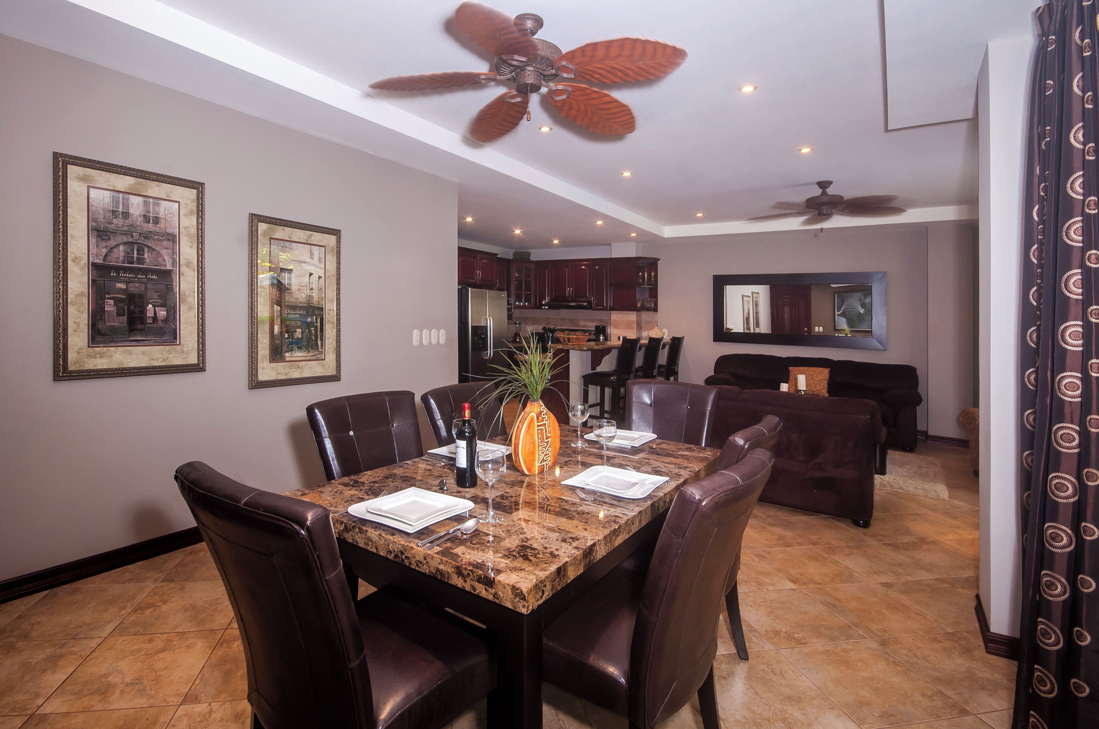 A dining area with a marble table, dark leather chairs, and a ceiling fan.