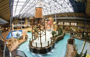 An indoor water park with a central water feature, slides, and a covered area with seating. - Rustic Penthouse Condo with Large Community Spa Room. (Kellogg)
