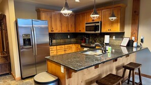 Uma cozinha moderna com armários de madeira, eletrodomésticos de aço inoxidável, bancadas de granito e iluminação pendente.