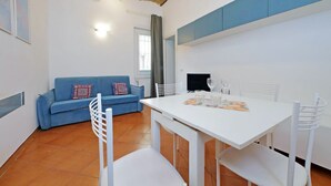 A modern living room with a blue sofa, white dining table, and chairs.