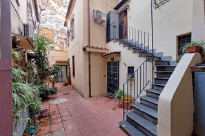 Une ruelle étroite avec un escalier menant à l’entrée d’un immeuble, bordée de plantes en pot et d’un chemin pavé.