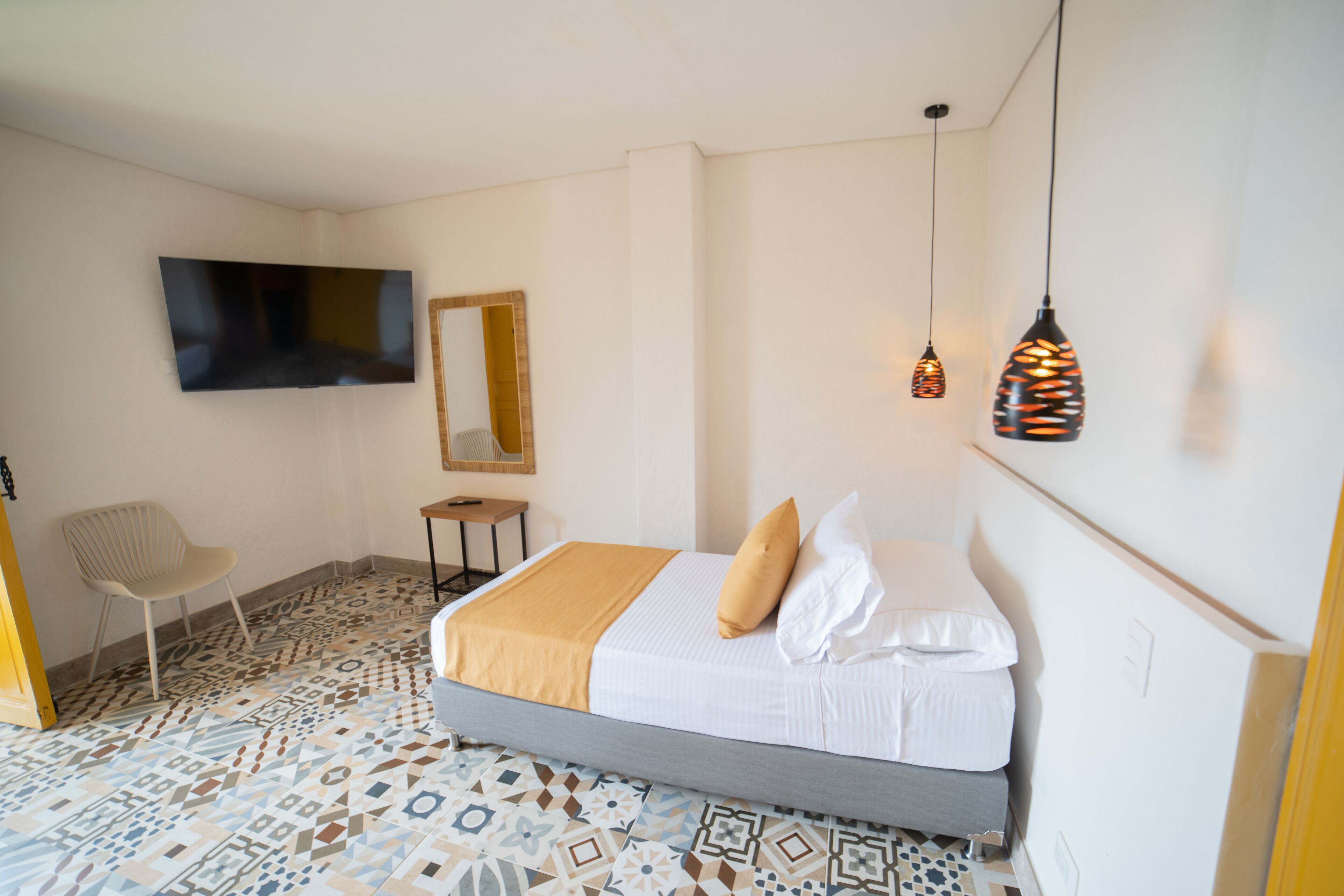 Una camera da letto con un letto, una TV a muro, una sedia e piastrelle decorative.